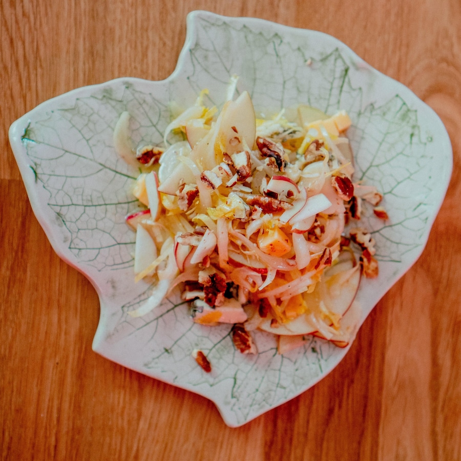 Une salade d'endive, pomme, pacane sur une assiette en forme de feuille d'érable.