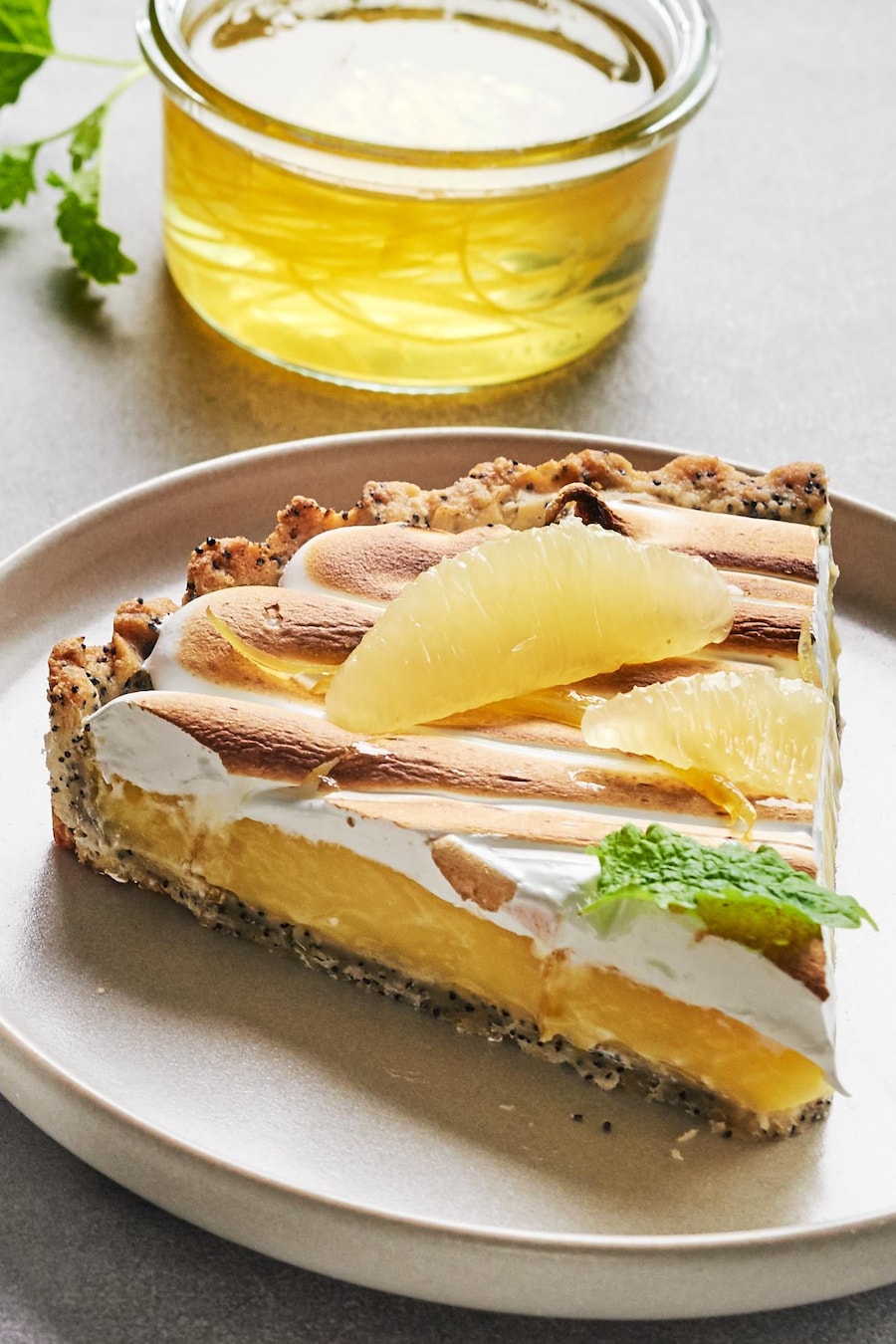 Une tarte au citron et au pavot dans une assiette avec un morceau déjà coupé dans une autre assiette.