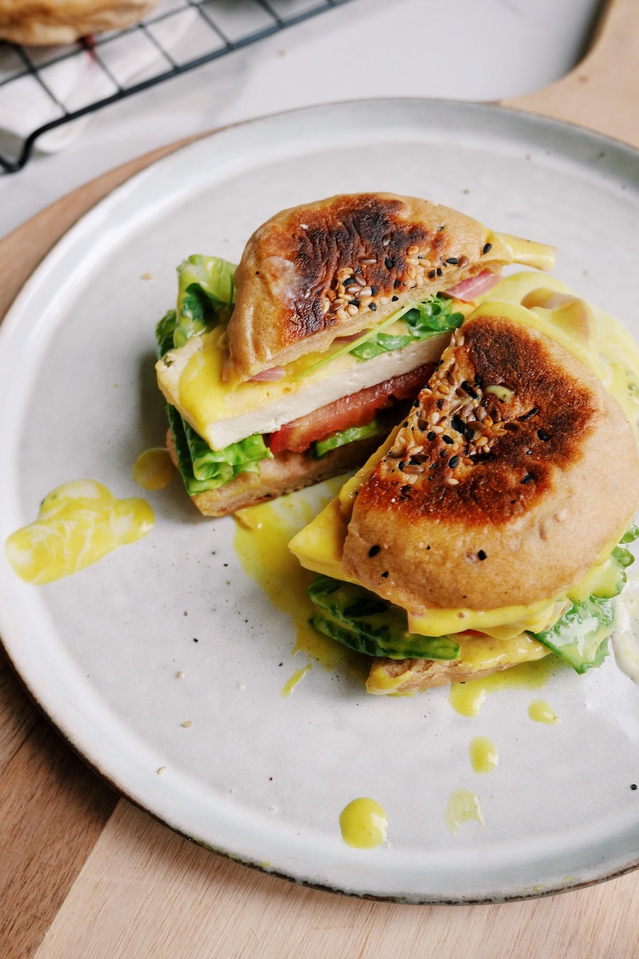 Un sandwich déjeuner végétalien coupé en deux dans un assiette posée sur une planche en bois.