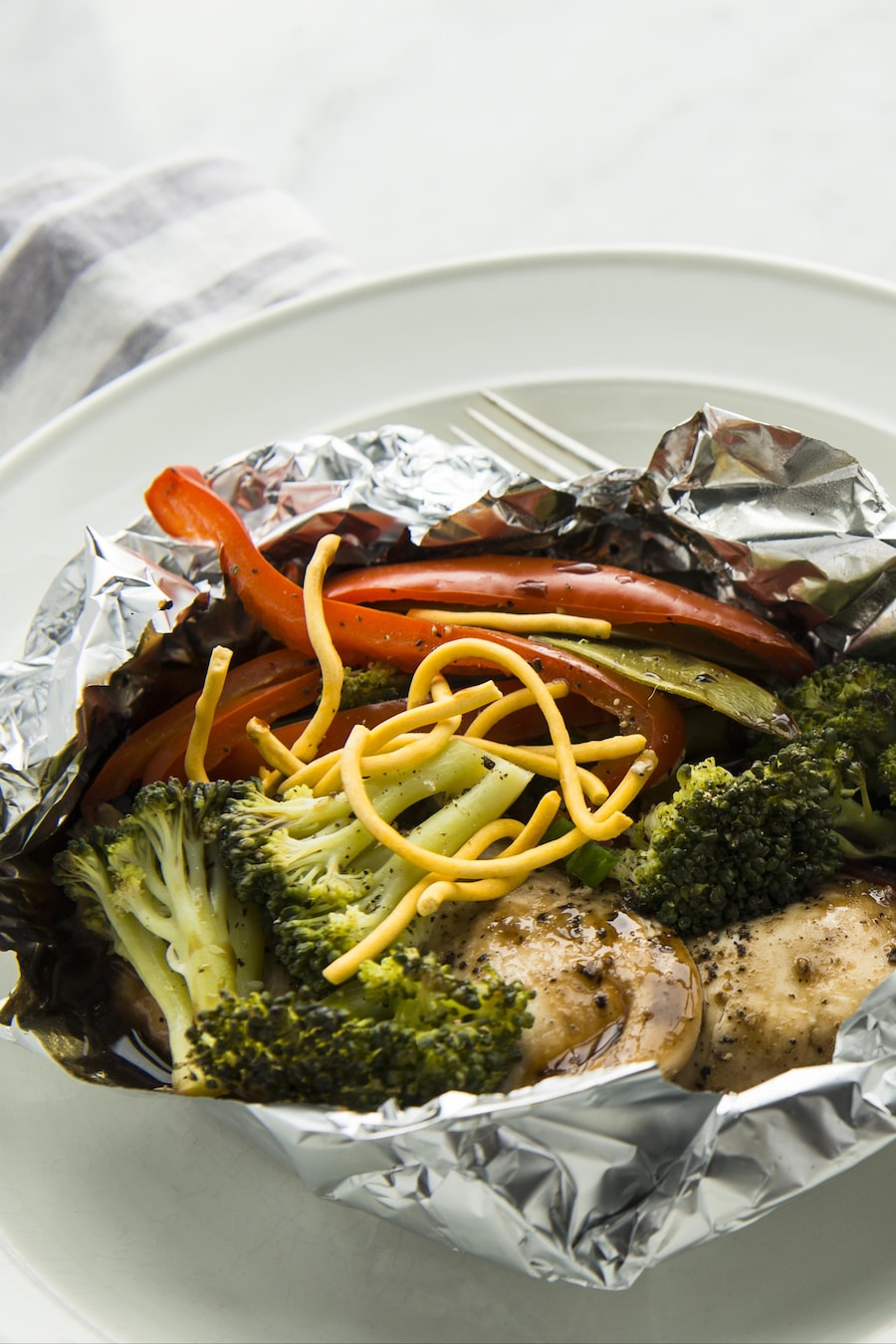Papillote de poulet avec légumes dans un papier d'aluminium servi dans une assiette.
