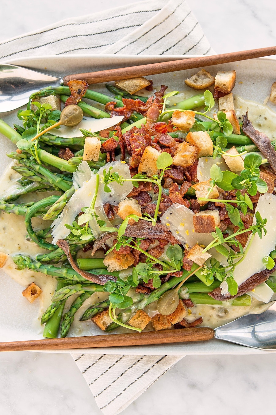 Des asperges avec tous les ingrédients du salade César dans une assiette de service.