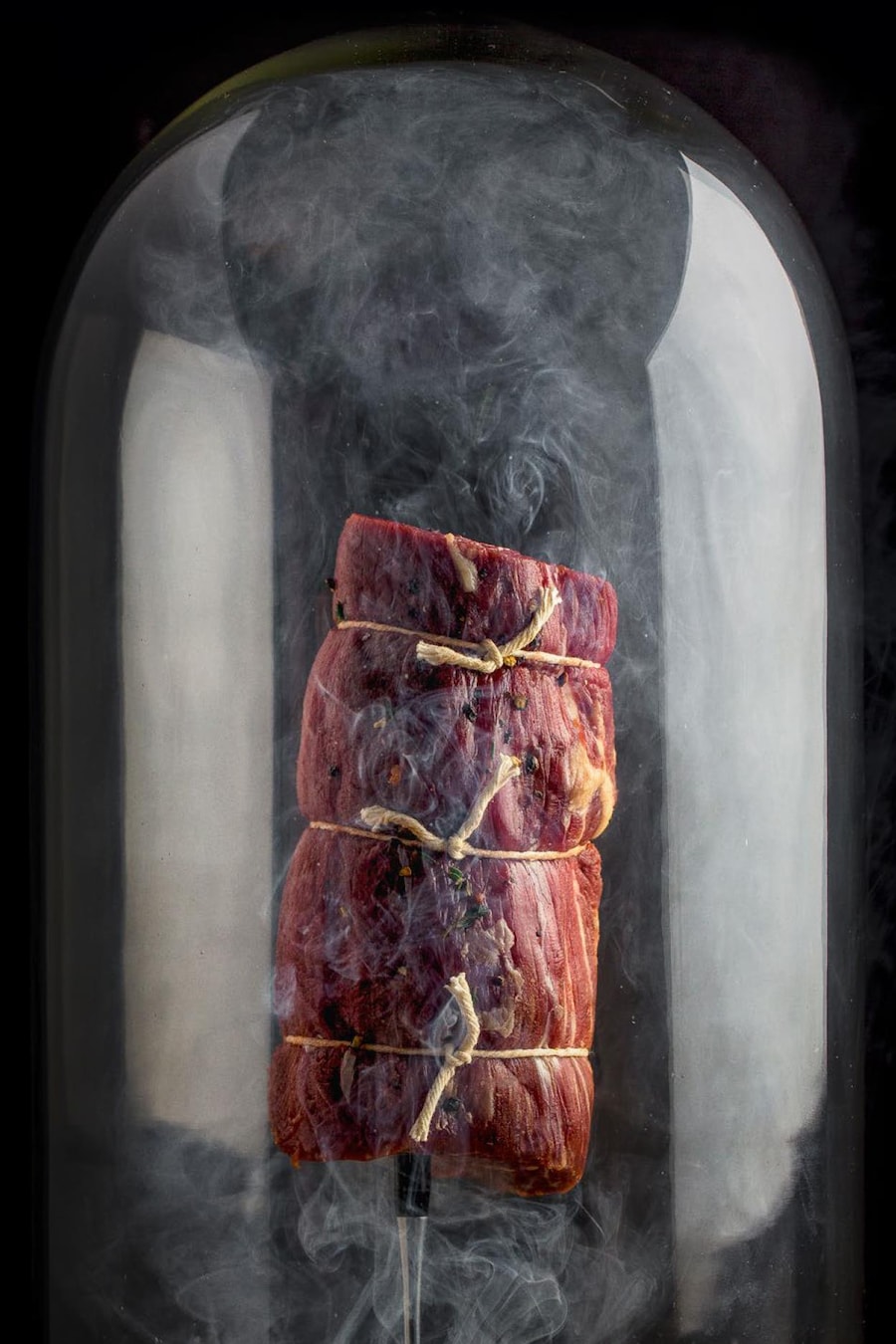 Une pièce de bœuf sous une cloche de verre avec de la fumée.