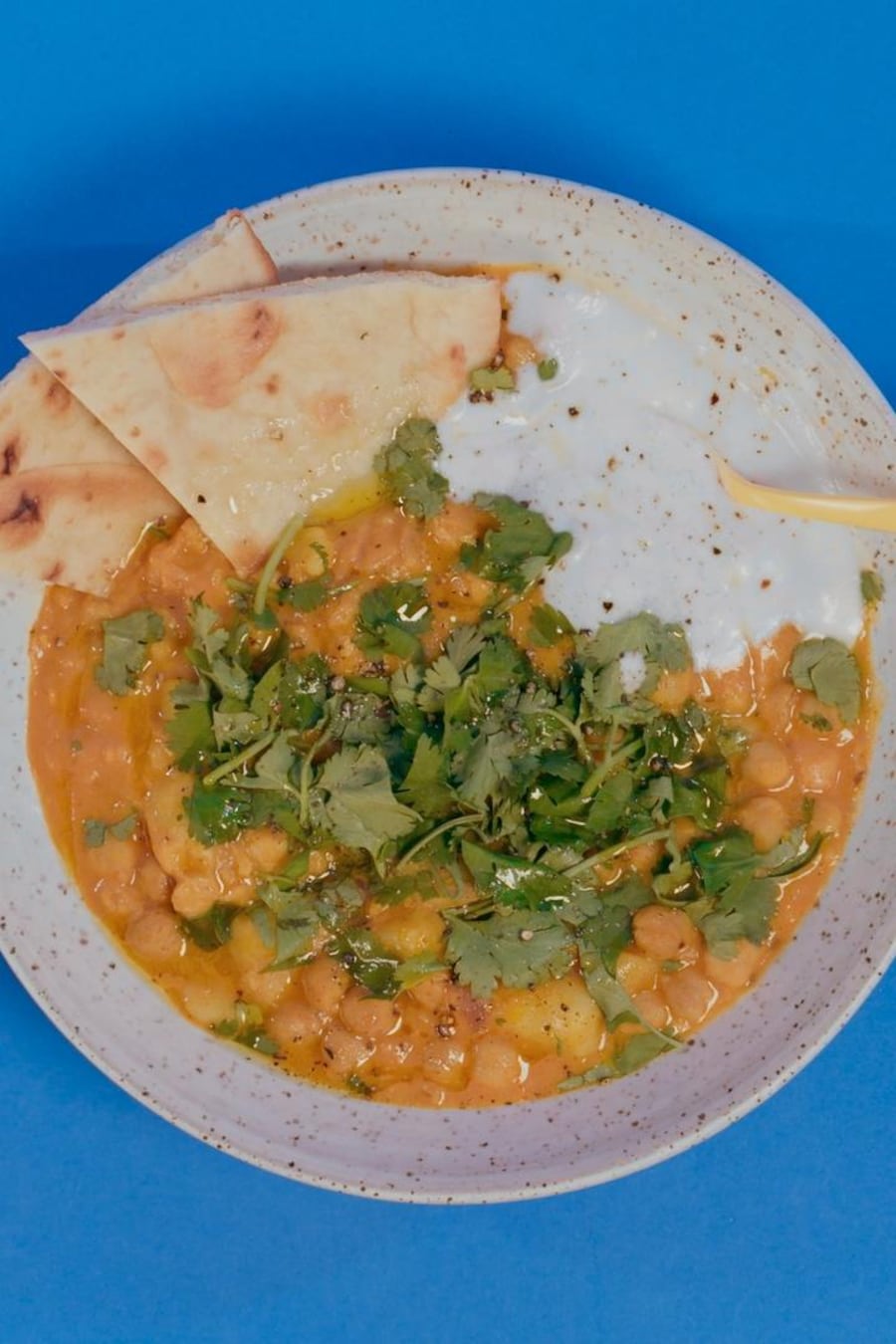 Un bol de curry de pois chiches avec de la coriandre, sauce blanche et pain naan.