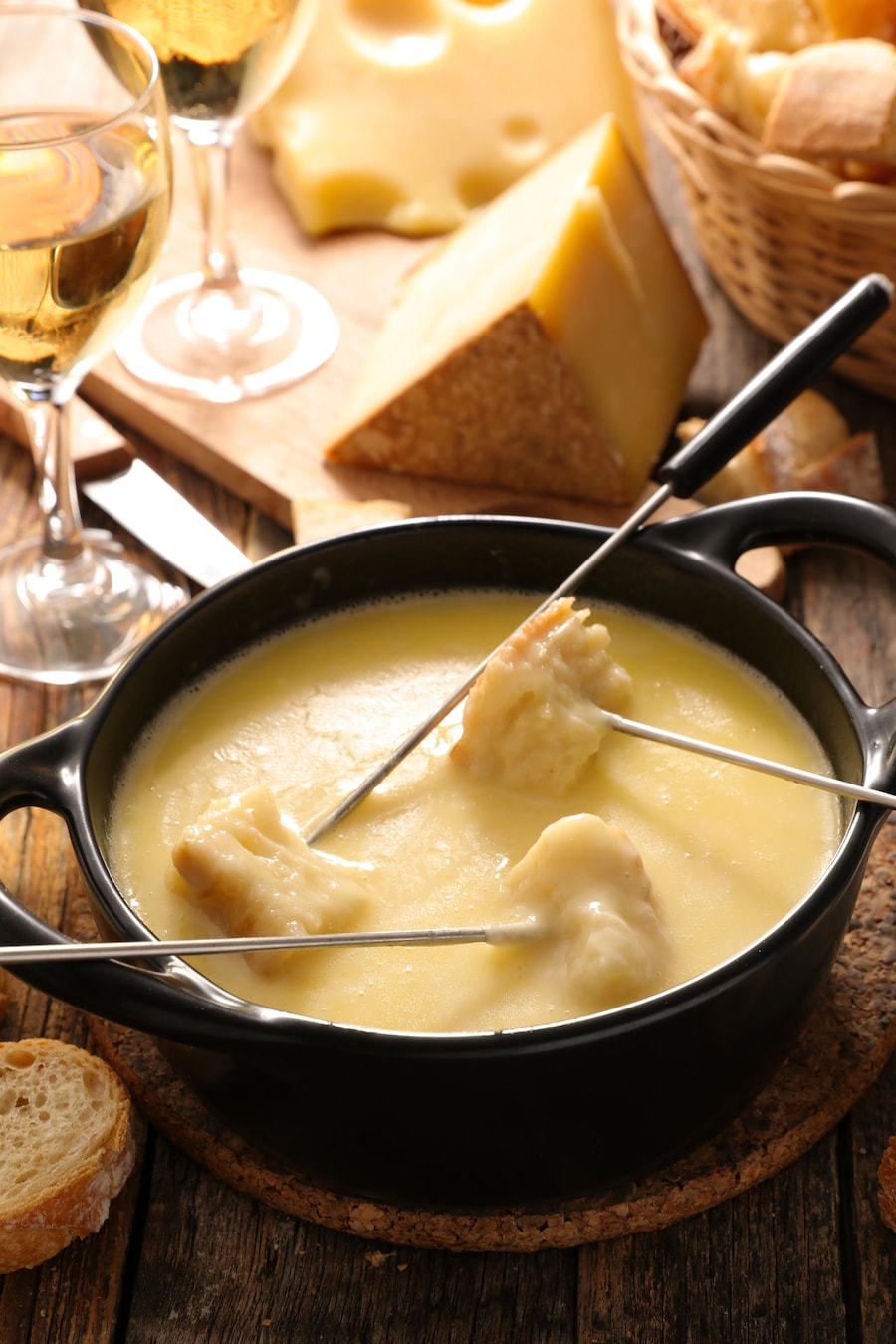 Une fondue au fromage avec deux verres de vin blanc et du pain baguette.