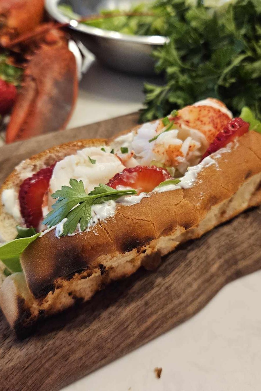 Un pain à hot-dog garni de homard, de tranches de fraises, d'herbes fraîches et garni de sauce au yogourt.
