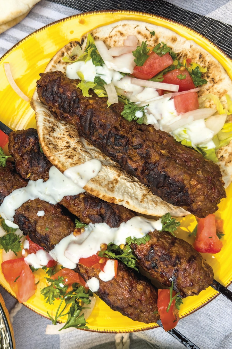 Des kebabs dans une assiette avec un pain pita, des morceaux de tomates et d'oignons et de la sauce.