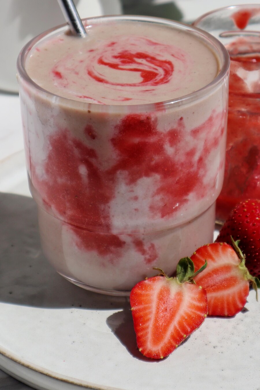 Un smoothie tourbillonnant de crème et de coulis de fraises dans un verre, à côté d'un pot de confiture de fraises.