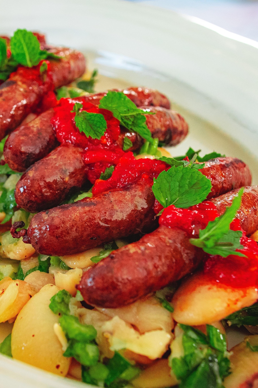 Des saucisses merguez grillées sur un lit de salade de haricots de Lima et céleri. Le tout est garni de harissa et de menthe ciselée.