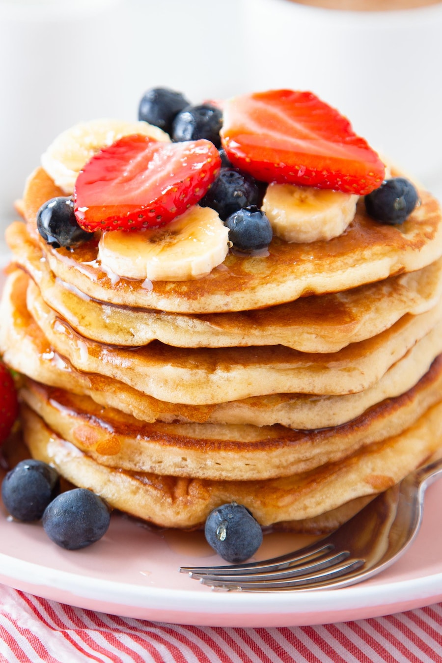 Des pancakes dans une assiette avec des bleuets, des fraises et des bananes.