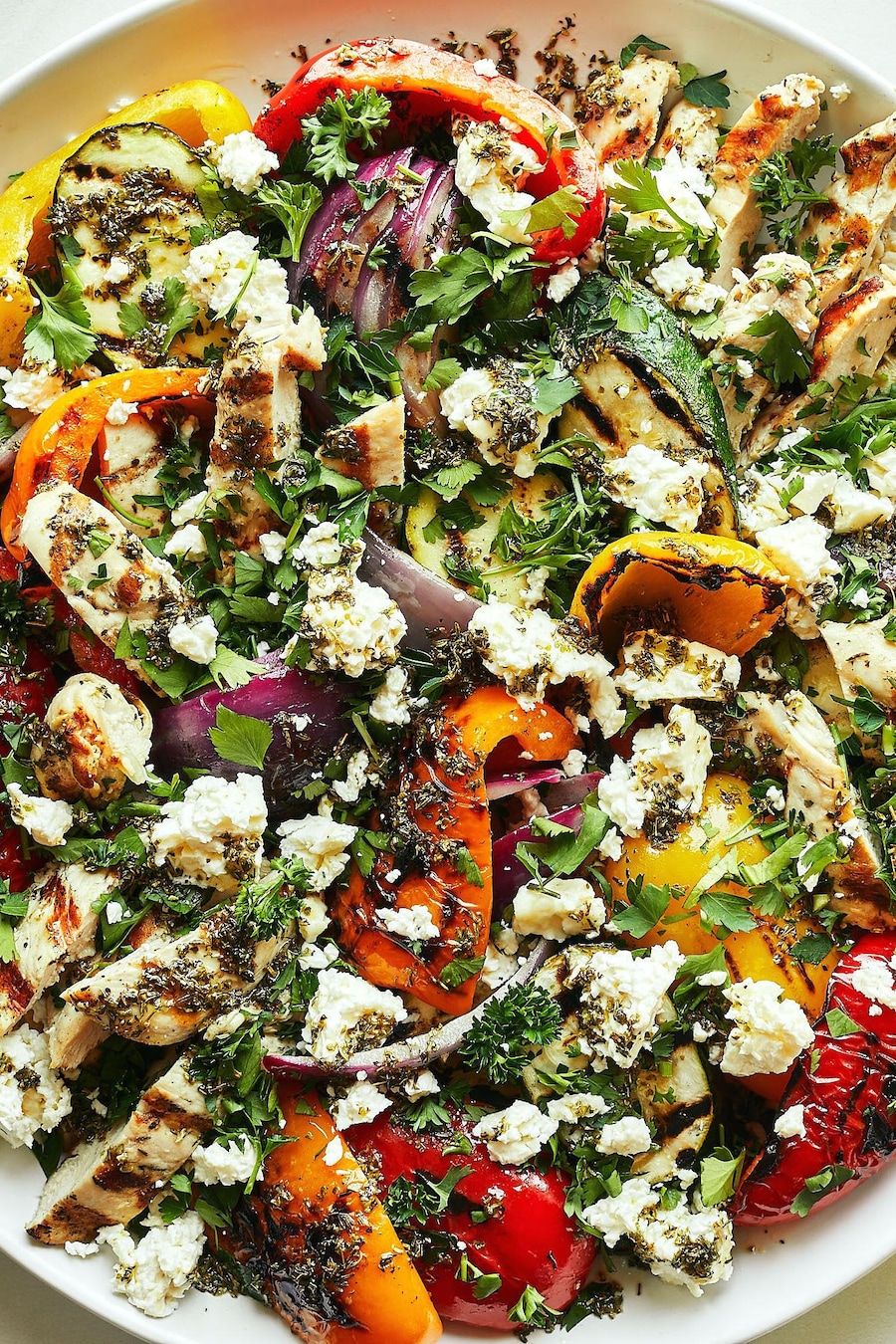 Une grande assiette déposée sur une table contenant du poulet et des légumes grillés à la grecque.
