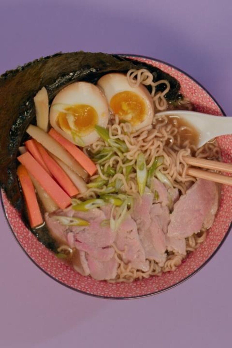 Un bol de soupe ramen au porc, servi avec des oeufs cuits dur, des carottes marinées et une feuille de nori.
