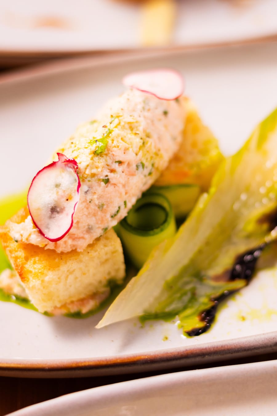 De la rillette de saumon dans une assiette avec des croûtons, des légumes croquants et une vinaigrette aux herbes.