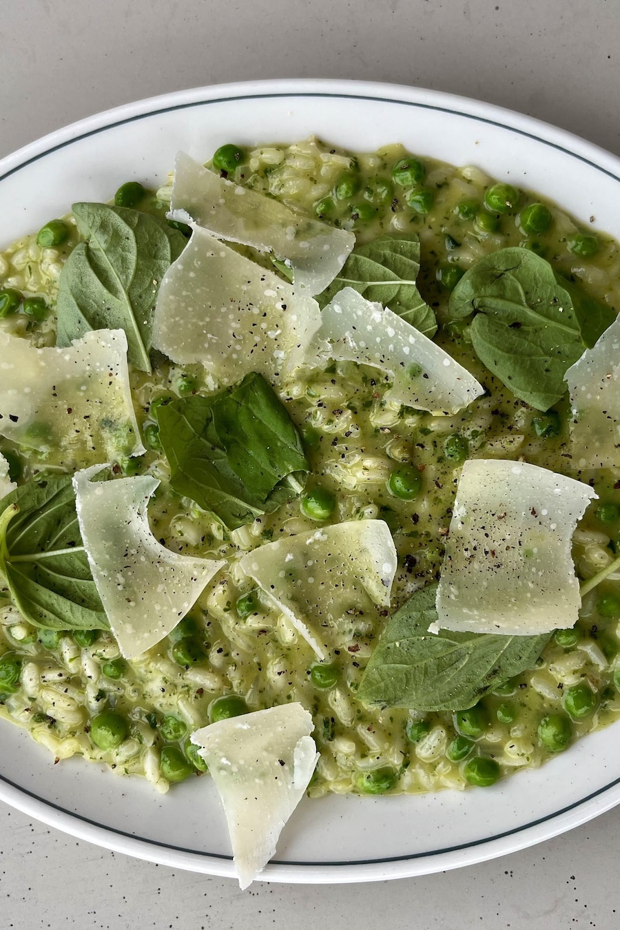 Un plat de risotto vert au basilic et à la roquette servi avec des petits pois et des copeaux de parmesan.