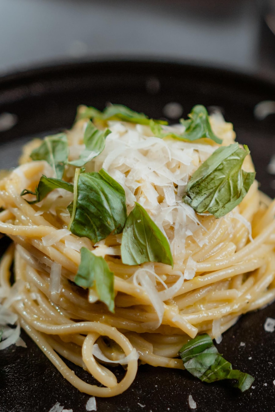Une petite quantité de spaghettis aux courgettes garnie de basilic et de fromage râpé.