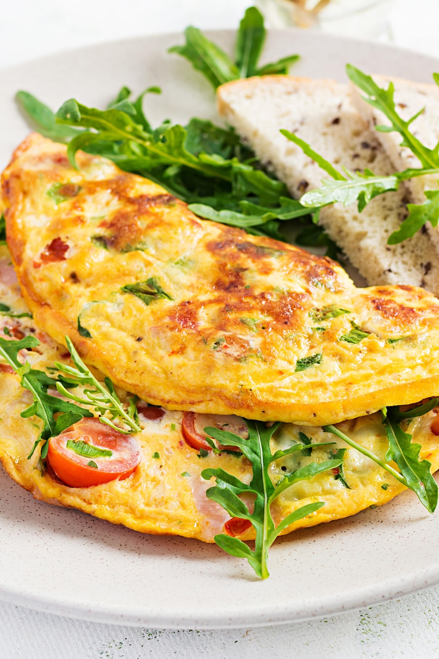 Dans une assiette, il y a une omelette contenant du jambon, des tomates cerises, du fromage ainsi que de la roquette.