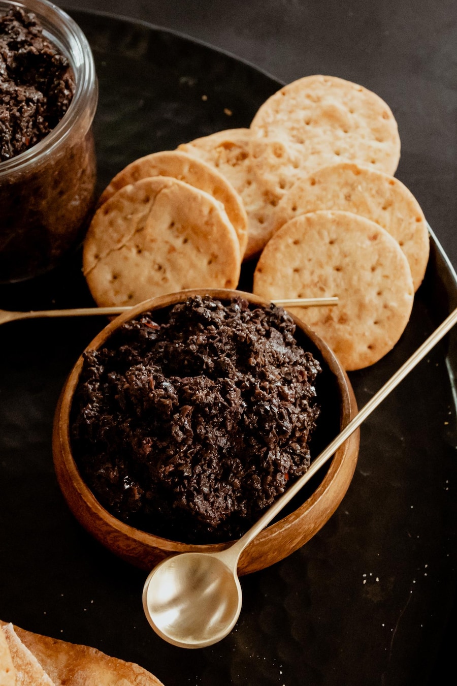 Deux bols remplis de tapenade aux olives noires avec de petits biscuits salés.