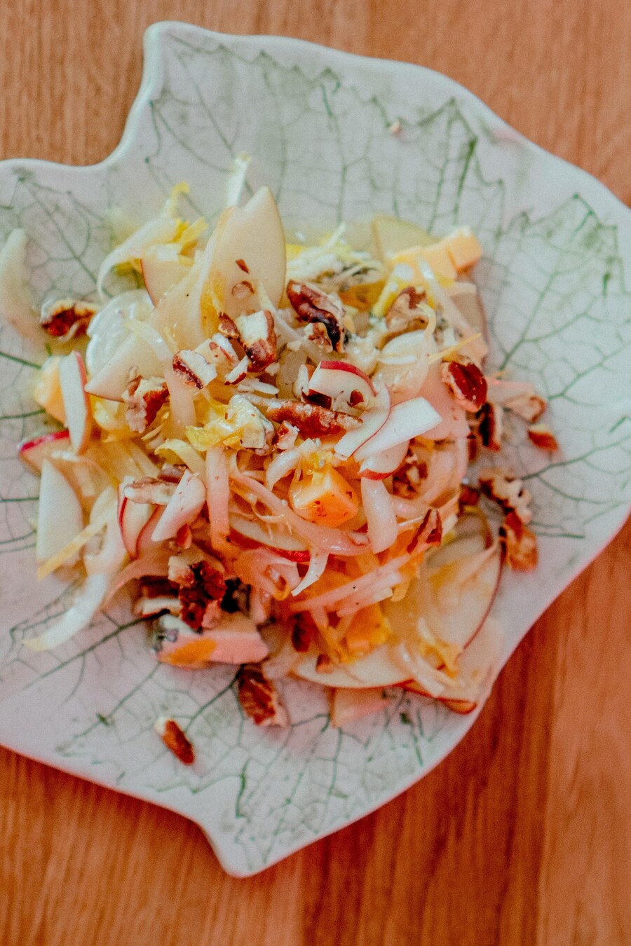 Une salade d'endive, pomme, pacane sur une assiette en forme de feuille d'érable.