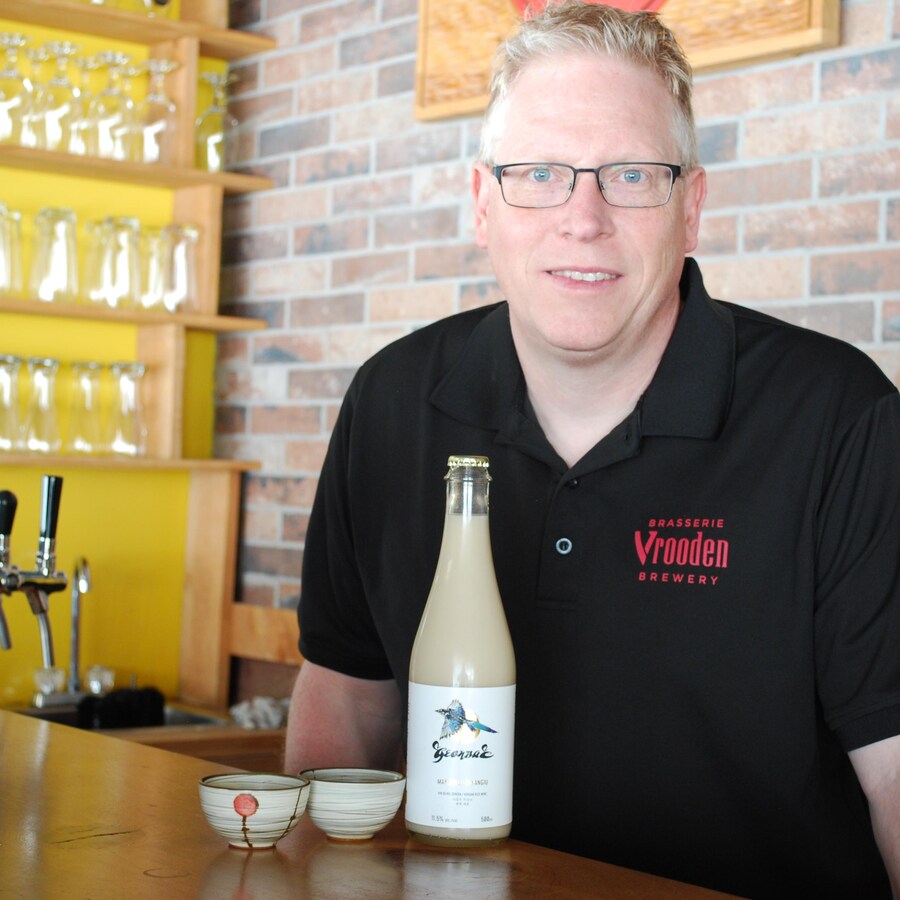 L'homme se tient derrière un bar. Une bouteille de makgeolli, un vin de riz à l'apparence laiteuse, est posée sur le bar, avec deux petits bols en céramique.