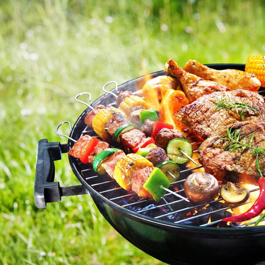 Des légumes, de la viande, des saucisses et des brochettes sur un barbecue au charbon.