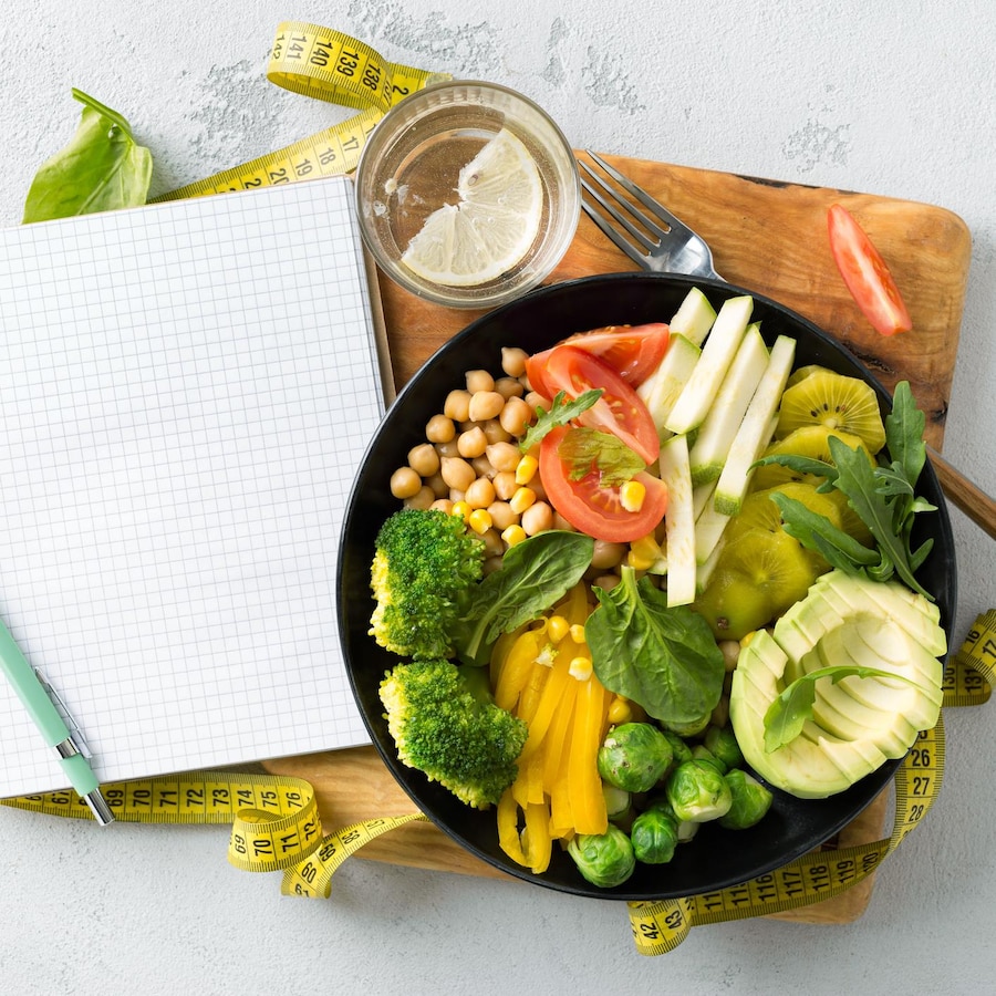 Une assiette remplie de légumes, avec un calepin de notes et un ruban à mesurer.