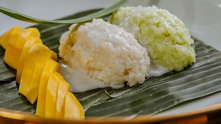 Deux boules de riz sont disposées dans une assiette à côté d'une mangue tranchée.