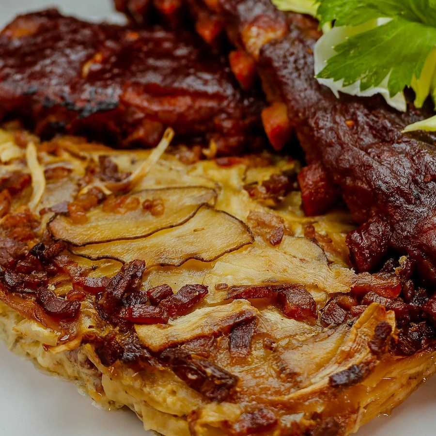 Un gratin de panais, pommes de terre rattes et bacon qui accompagne les côtes levées dans une assiette.