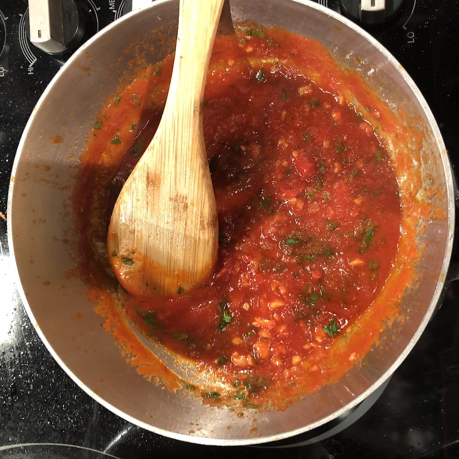 Un chaudron sur une plaque de cuisson contient une sauce tomate et une cuillère de bois