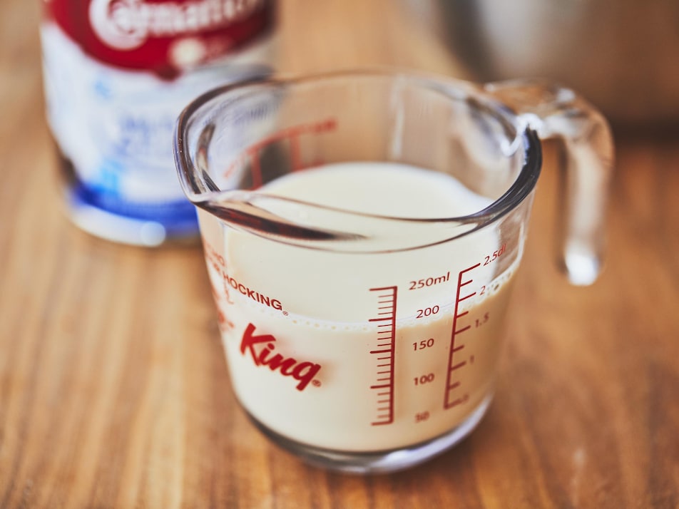 Une tasse à mesurer en verre remplie de lait sur une surface en bois. 