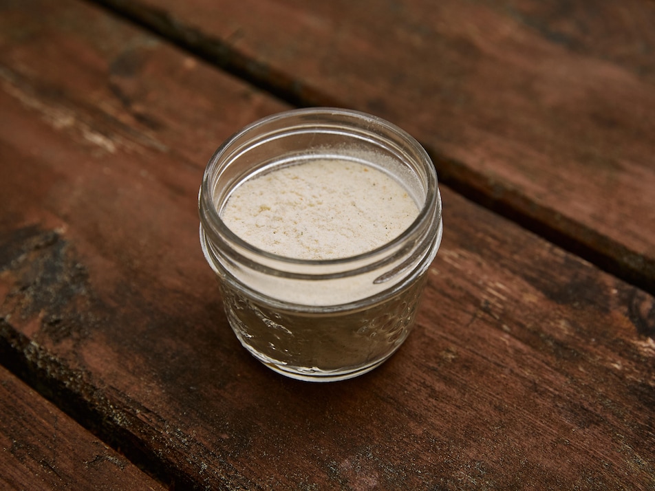 Un petit pot en verre contenant du bouillon déshydraté, est déposé sur une table de bois.