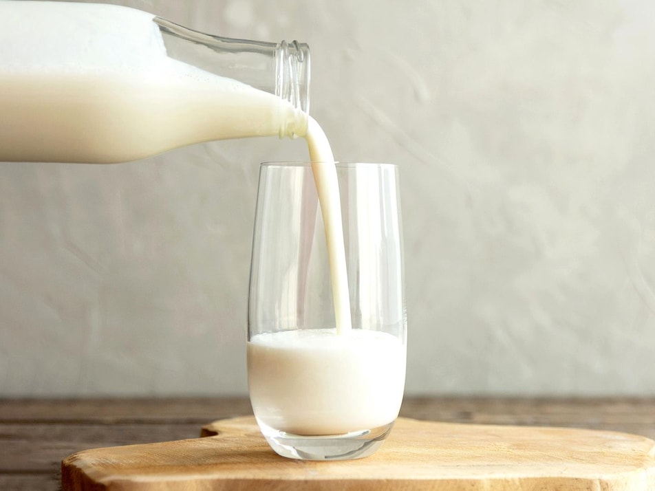 Un bouteille de lait qui se verse dans un verre en vitre.