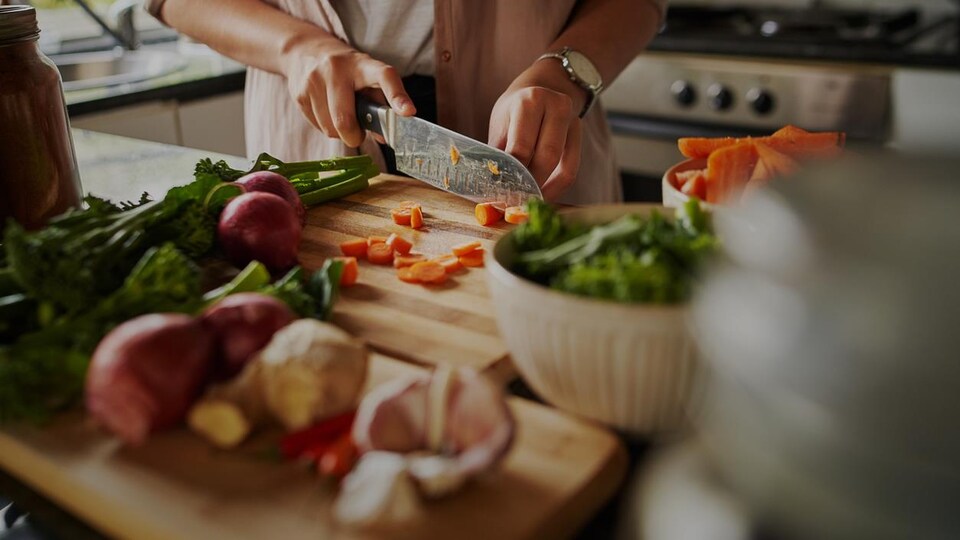 Des carottes se font découper sur un comptoir, sur une planche à découper.