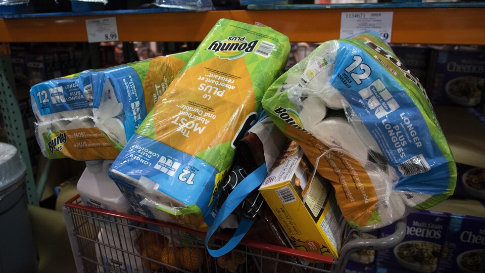 Un panier d'épicerie rempli de paquets d'essuie-tout et de produits alimentaires.