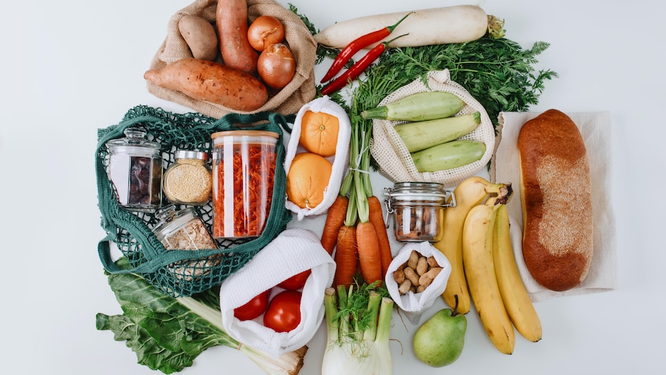 Des fruits, légumes, pains et conserves sont disposés sur un fond blanc. 