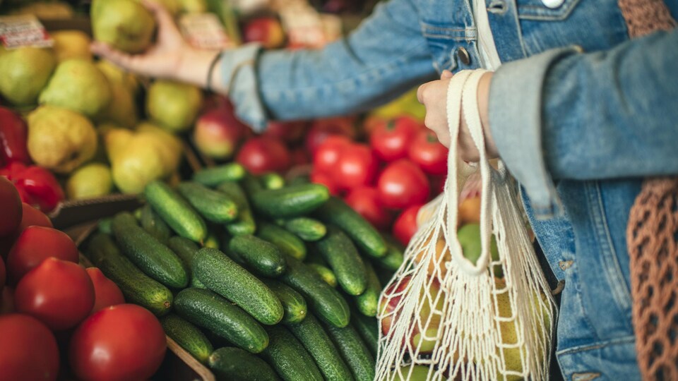 Une personne rempli un sac réutilisable de légumes à partir d'un étal de légumes de marché.