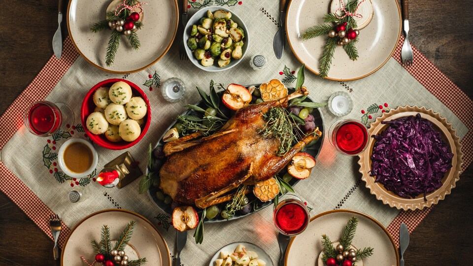 Vue de dessus du dîner de Noël traditionnel servi sur table. Menu du réveillon de Noël de canard rôti, boulettes et chou rouge avec du vin rouge sur une table à manger décorée.