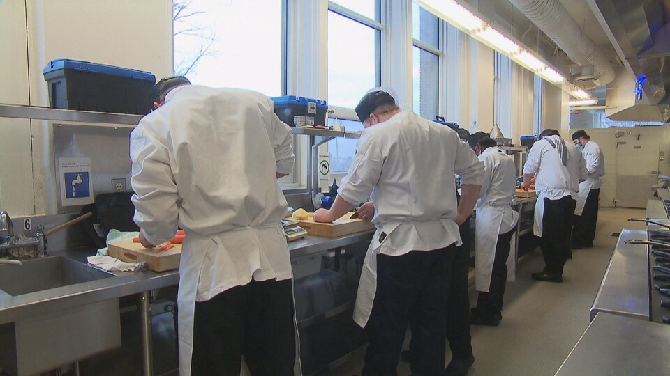 Des cuisiniers de dos devant un plan de travail.