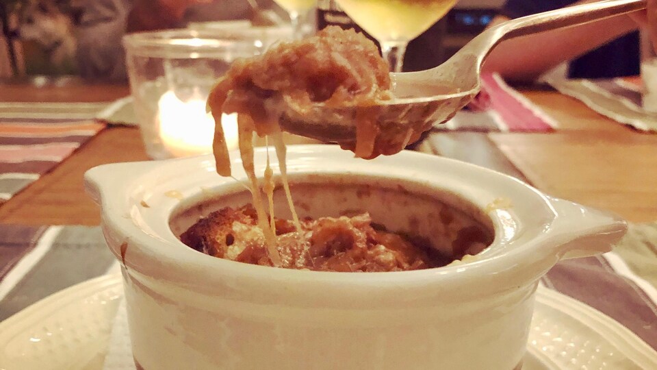 Un bol de soupe à l'oignon, une cuillère, des gens et verres de vin. 