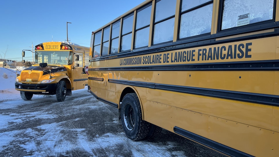Deux autobus scolaires arrivent dans une école.