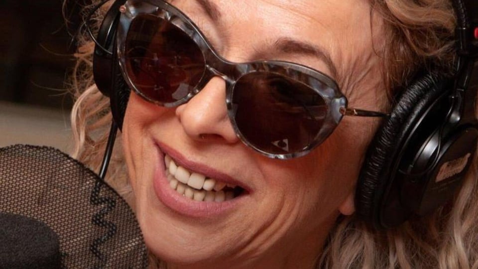 En studio, la chanteuse sourit, lunettes fumées sur le nez.