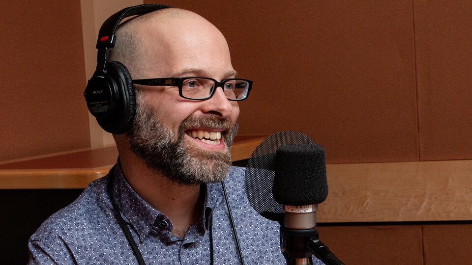 En studio, l'homme chauve à lunettes sourit à l'animatrice.