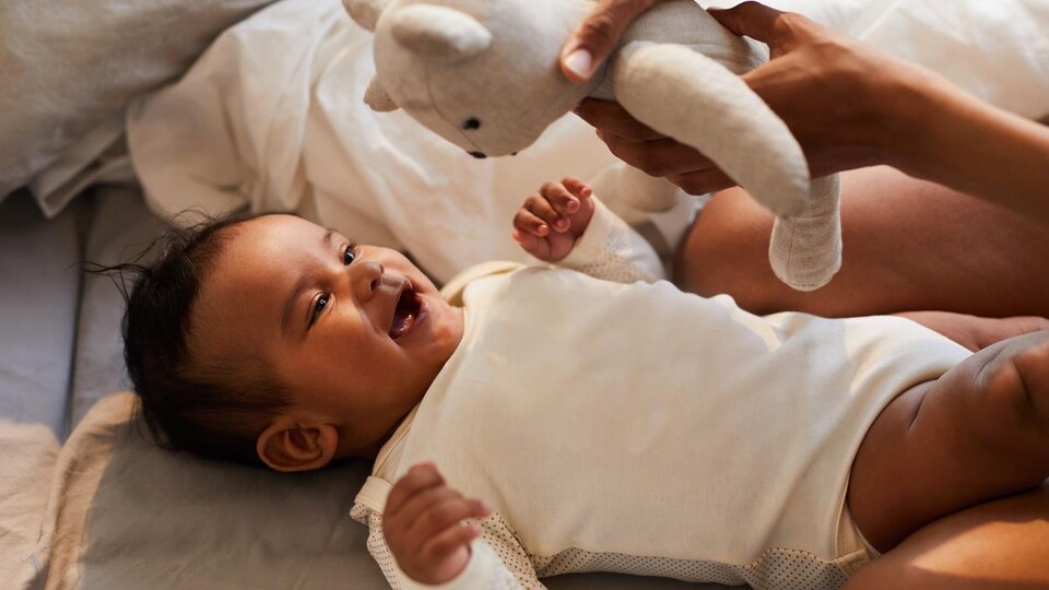 Close-up of mother showing toy bear to black baby boy lying on bed and having fun from game