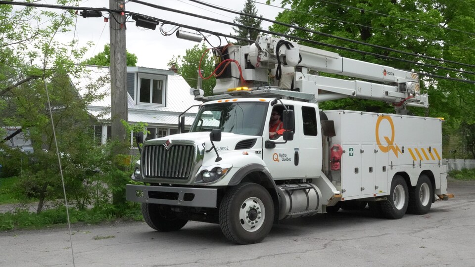 Un camion d'Hydro-Québec sous les câbles électriques devant une résidence. 