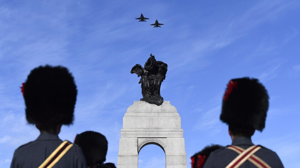 Des militaires en uniforme d'apparat observent le passage de deux avions CF-18 au-dessus du Monument commémoratif de guerre du Canada.