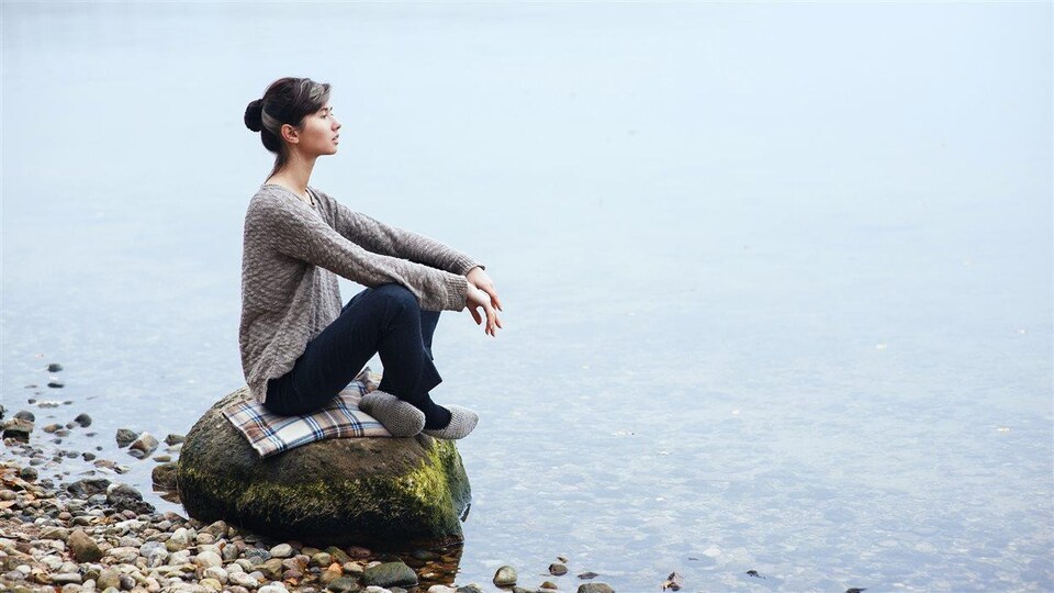 Une femme assise au bord d'un lac regarde au loin d'un air calme et serein.