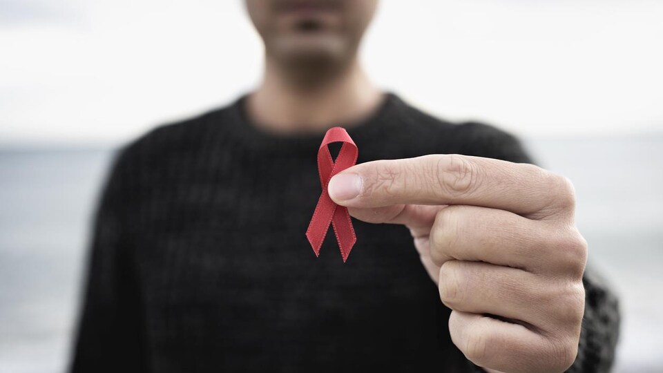 Un homme tient un ruban rouge, le symbole de la lutte contre le sida, du bout de ses doigts. 