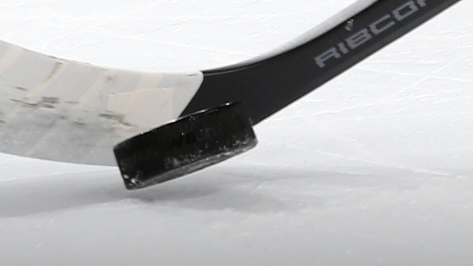 Gros plan sur un bâton de hockey et une rondelle sur la glace