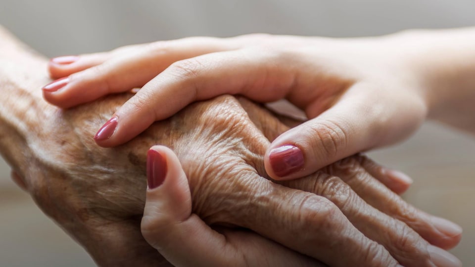 Une femme plus jeune tient la main d'une femme âgée.