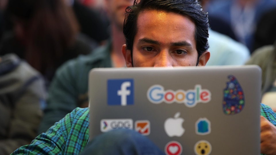 Un homme utilise son laptop avec des autocollants de Facebook et Google.
