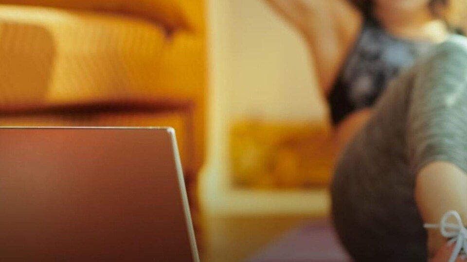 Une femme fait des abdos sur un tapis de yoga dans son salon en regardant un écran d'ordinateur.