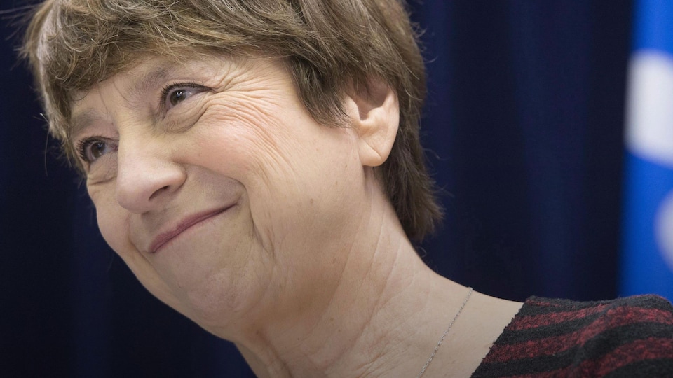 Françoise David en gros plan sourit alors qu'elle est est posée devant un drapeau du Québec.